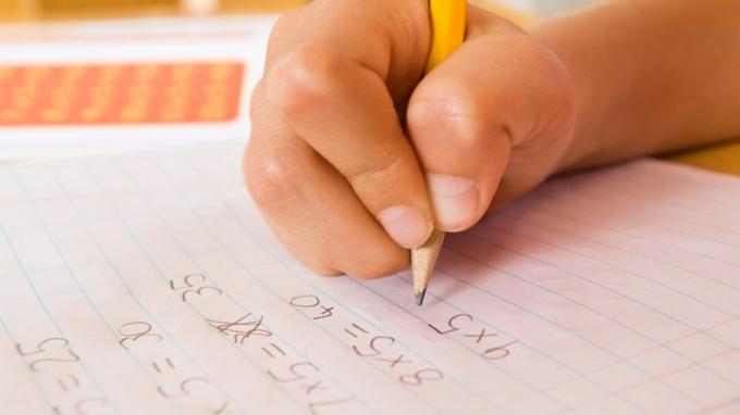 Lapse käsi, kes täidab kodutöö matemaatikaülesannete abil